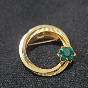 Mid-century modern gold-tone circle brooch with an emerald green rhinestone. 